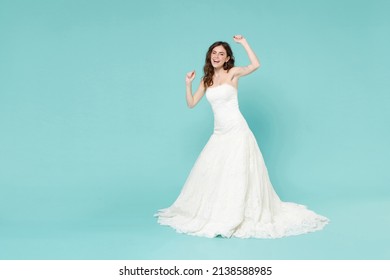 Full length of joyful bride young woman in white wedding dress doing winner gesture clenching fists dancing isolated on blue turquoise background studio portrait. Ceremony celebration party concept