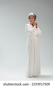 Full Length Of Joyful Middle Aged Bride In White Wedding Dress Standing On Grey