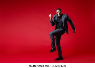 Full Length Of Joyful Young African American Business Man 20s Wearing Classic Jacket Suit Standing Doing Winner Gesture Clenching Fists Isolated On Bright Red Color Wall Background Studio Portrait