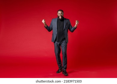 Full Length Of Joyful Young African American Business Man 20s Wearing Classic Jacket Suit Standing Doing Winner Gesture Clenching Fists Isolated On Bright Red Color Wall Background Studio Portrait