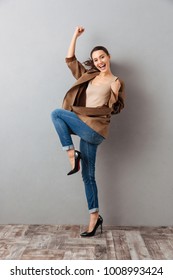 Full length of a joyful young asian woman celebrating success over gray background