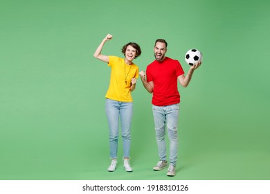 Full Length Joyful Young Couple Friends Sport Family Woman Man Football Fans In Yellow Red T-shirts Cheer Up Support Favorite Team With Soccer Ball Doing Winner Gesture Isolated On Green Background