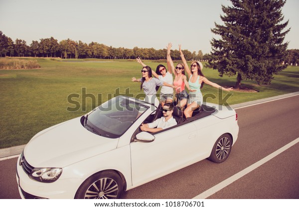 Full length of ladies and guy driver, chics\
girlfriends express emotions, success, feel wind. Five funky\
tourists on trip, auto rent, transport, inspiration journey, cap\
hats, glasses, laugh,\
relax