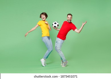 Full Length Of Laughing Couple Friends Sport Family Woman Man Football Fans In T-shirts Cheer Up Support Favorite Team With Soccer Ball Standing On Toes Spreading Hands Isolated On Green Background