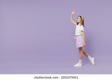 Full Length Little Fun Smiling Happy Kid Girl 12-13 Years Old In White Shirt Walk Going Strolling Waving Hand Isolated On Purple Color Background Children Studio Portrait. Childhood Lifestyle Concept