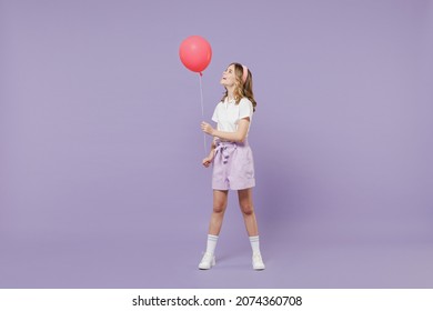 Full length little kid girl 12-13 year old in white shirt celebrate birthday holiday party hold colorful air inflated helium balloon isolated on purple background Childhood children lifestyle concept