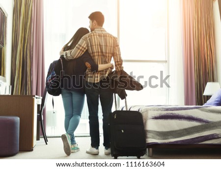 Full length of loving young couple looking through window in hotel room. Family on honeymoon