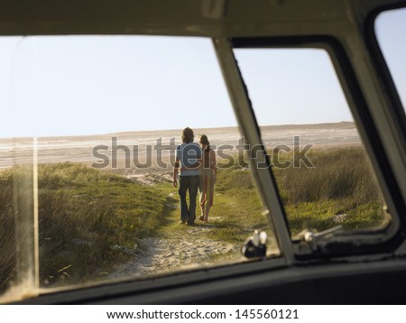 Full length of loving young couple walking towards beach view from campervan window