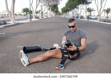 Full length of male athlete in gray t shirt and black shorts sitting on asphalt road and putting on prosthetic leg before running on city street - Powered by Shutterstock