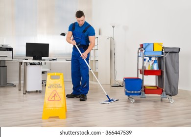 Full Length Of Male Janitor Mopping Floor In Office