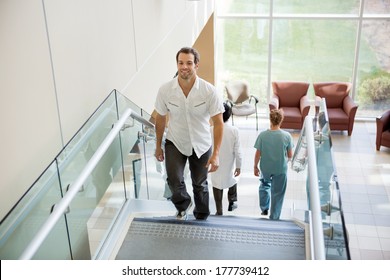 Full Length Male Patient And Medical Team Walking On Stairs In Hospital