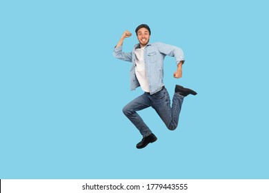Full length, man in denim outfit flying and jumping in air with inspired ambitious expression, taking big step and hurrying, running to final sale. indoor studio shot isolated on blue background - Shutterstock ID 1779443555