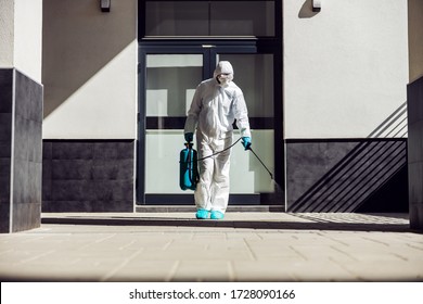 Full length of man in sterile uniform and mask sterilizing surface outdoors from corona virus, fungus and disease. - Shutterstock ID 1728090166