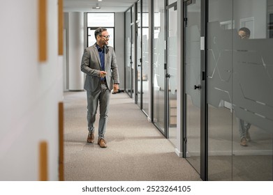 Full length of marketing manager in eyeglasses looking away and walking in modern office corridor - Powered by Shutterstock