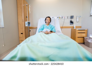 Full length of mature male patient using mobile phone on bed in hospital - Powered by Shutterstock