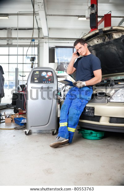 Full length of mechanic discussing repairs with\
customer on phone