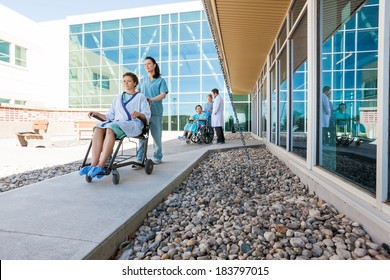 Full Length Of Medical Team With Patients On Wheelchairs At Hospital Courtyard