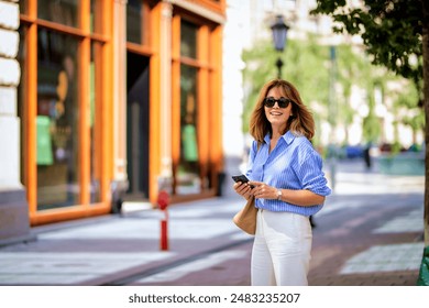 Full length of mid aged woman walking on city street. Blone haired female wearing blue shirt with white pants.  - Powered by Shutterstock