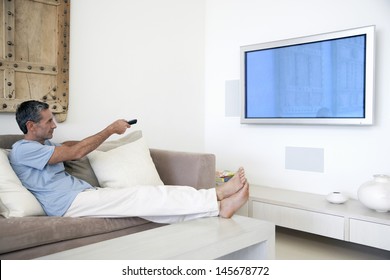 Full Length Of Middle Aged Man Using TV Remote In Living Room