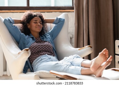Full length millennial African American woman homeowner daydreaming in comfortable armchair with legs on footstool, breathing fresh air, sleeping resting, enjoying peaceful leisure time at home. - Powered by Shutterstock