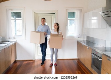 Full length millennial wife and husband hold carton boxes with belongings standing in modern kitchen at home. Attractive happy couple bought new house. Moving relocate day mortgage and tenant concept - Powered by Shutterstock