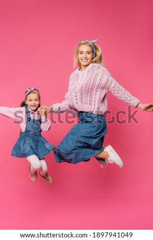 full length of mother and kid smiling and jumping on pink