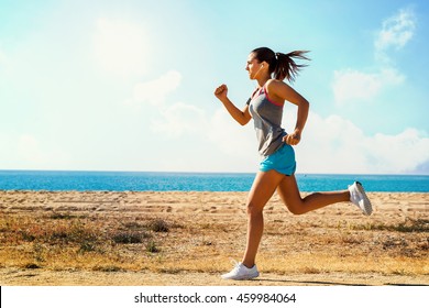 Full length in motion shot of attractive young woman jogging along beach front on sunny morning. - Powered by Shutterstock