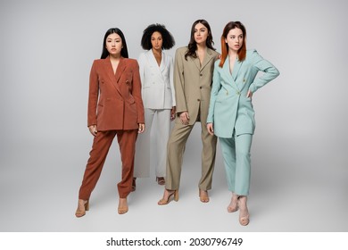 Full Length Of Multiethnic Group Of Models In Pastel Color Suits Posing On Grey