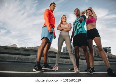 Full length of multi-ethnic group of people standing outdoors on the city street after workout. Fitness group standing together after workout and looking at camera. Low angle shot.