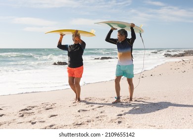 Full length of multiracial senior couple carrying surfboards on heads while walking at sunny beach. water sport and active lifestyle. - Powered by Shutterstock