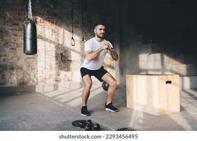 Full length of muscular man in sportswear doing squats during intense training at modern sports center with fitness equipment for workout