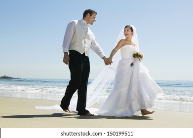 Full length of newlywed couple holding hands while walking on beach - Powered by Shutterstock