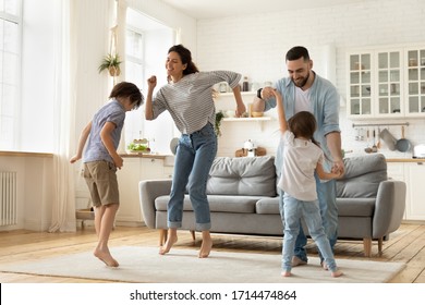 Full length overjoyed family of four jumping to music in modern studio living room. Excited young married couple dancing with playful little children siblings, spending active free time at home. - Powered by Shutterstock