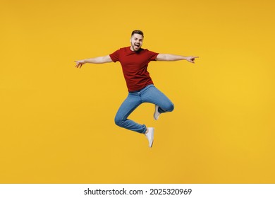 Full Length Overjoyed Fun Happy Young Man Wear Red T-shirt Casual Clothes Jump High With Outstretched Hands Isolated On Plain Yellow Color Wall Background Studio Portrait. People Lifestyle Concept.