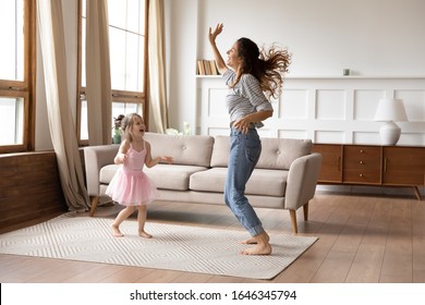 Full length overjoyed little preschool child girl in princess wear spending active weekend time with happy young mother. Crazy energetic family of two dancing together to music in living room.