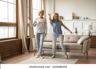 Full length overjoyed middle aged grey haired elderly woman dancing to energetic music with grown up blonde daughter. Happy smiling two generations female family having fun together in living room. - Powered by Shutterstock