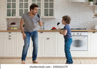 Full length overjoyed young father with happy little school age boy son holding soup ladles as microphones, singing, dancing, having fun, enjoying family weekend together in modern kitchen at home. - Powered by Shutterstock