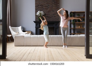Full length overjoyed young mother dancing to favorite energetic music with little cute adorable smiling daughter in living room. Happy family of two enjoying active time on weekend at home.