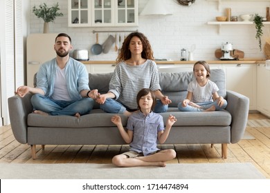 Full length peaceful calm couple practicing yoga exercises with small children in studio living room. Mindful little boy sitting on floor in lotus pose while parents relaxing on sofa with sister. - Powered by Shutterstock