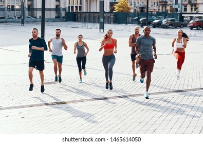 Full length of people in sports clothing jogging while exercising on the sidewalk outdoors                      