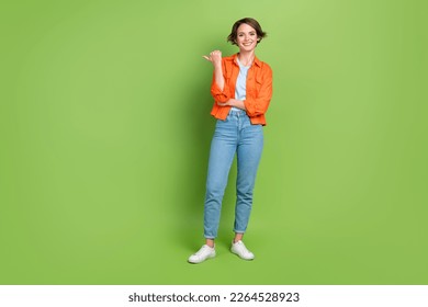 Full length photo of adorable cute woman wear denim jacket pointing thumb empty space isolated green color background - Powered by Shutterstock