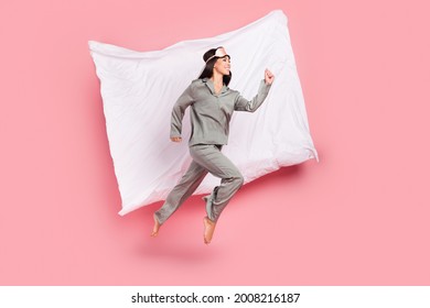 Full length photo of adorable hurrying woman nightwear mask smiling jumping high running fast isolated pink color background