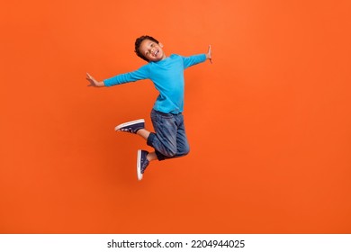 Full length photo of adorable little pupil boy jumping school shopping poster wear trendy blue clothes isolated on orange color background - Powered by Shutterstock