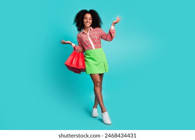 Full length photo of adorable lovely girl wear print shirt holding shoppers walking empty space isolated teal color background Stockfoto