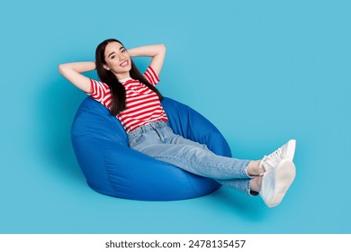 Full length photo of adorable lovely girl wear striped t-shirt relaxing bean bag arms behind head empty space isolated blue color background - Powered by Shutterstock