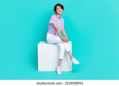 Full length photo of adorable pretty lady wear violet t-shirt smiling sitting white platform isolated turquoise color background - Shutterstock ID 2229038953