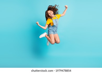 Full Length Photo Of Adorable Strong Small School Girl Wear Denim Jeans Overall Jumping Showing Muscles Isolated Blue Color Background