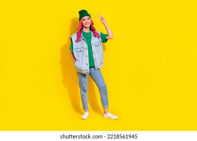 Full length photo of adorable sweet lady wear jeans waistcoat smiling showing v-sign isolated yellow color background