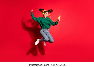 Full length photo of adorable young lady wear green knitted pullover listening music headphones dancing jumping isolated red color background - Powered by Shutterstock