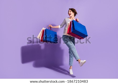 Full length photo of adorable young lady dressed casual clothes dancing holding colorful bargains isolated purple color background